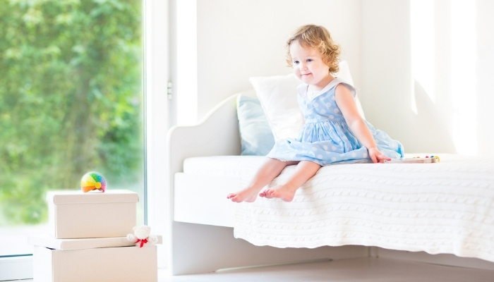 A cute little girl sitting on her white toddler bed.