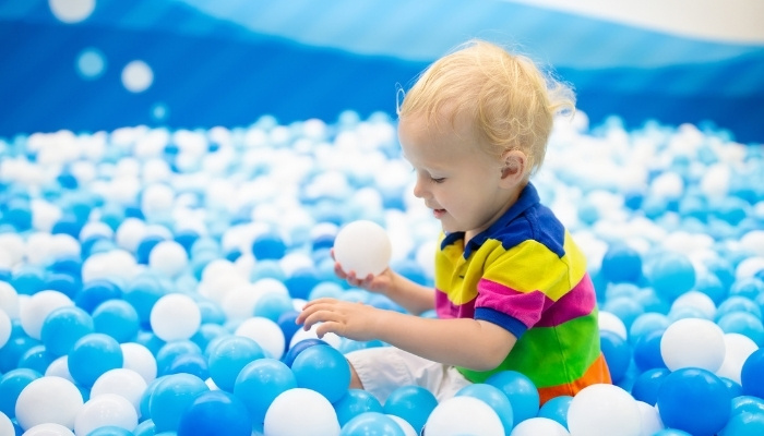 A little boy playing in a large ball pit by himself.