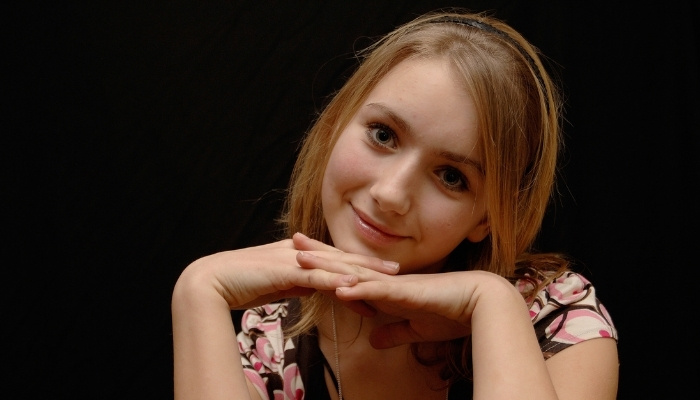 A smiling 12-year-old girl against a black background.