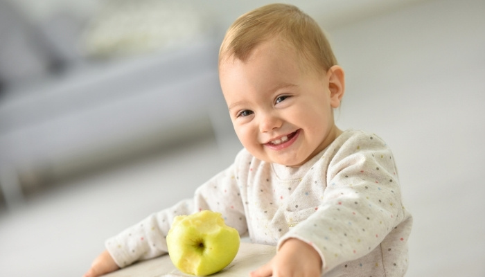 A cute 15-month-old girl smiling with a half-eaten apple in front of her.
