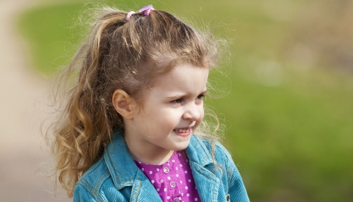 A cute 4-year-old girl standing outside in a purple shirt and corduroy jacket.