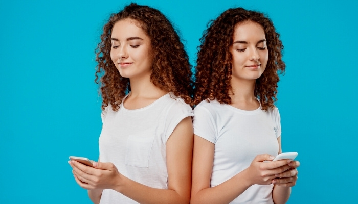 Teenage twin sisters holding cell phones against a blue background.