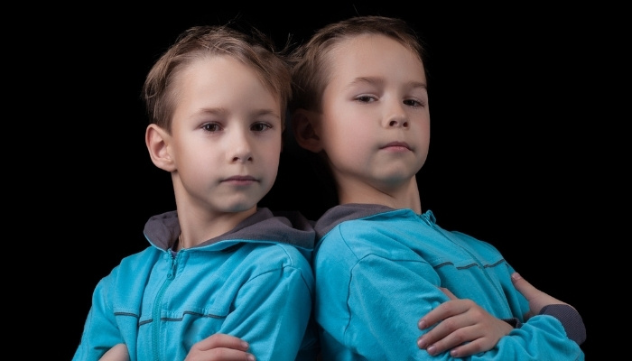 Twin brothers in blue shirts standing side by side with their arms crossed.