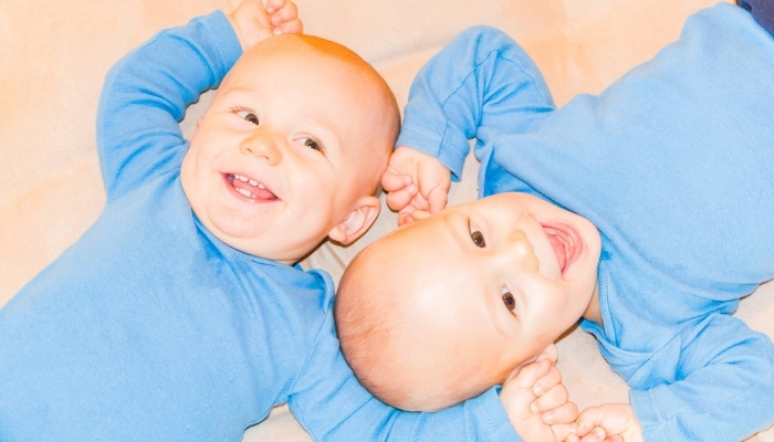 Twin toddler boys in blue outfits lying head to head.