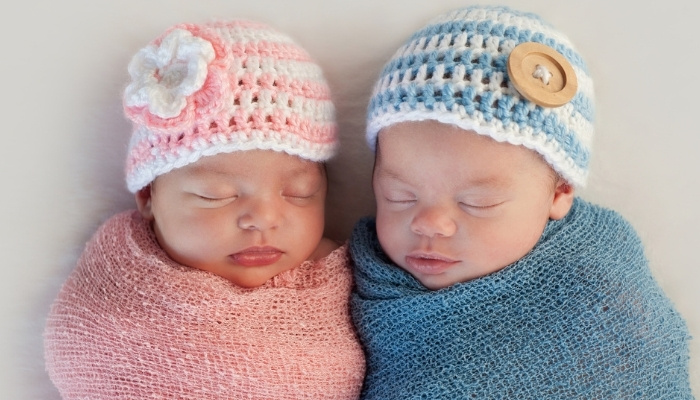 Boy and girl newborn twins in matching pink and blue hats and blankets.