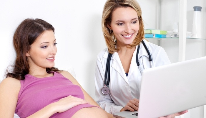 A pregnant lady at checkup looking at a laptop with her doctor.