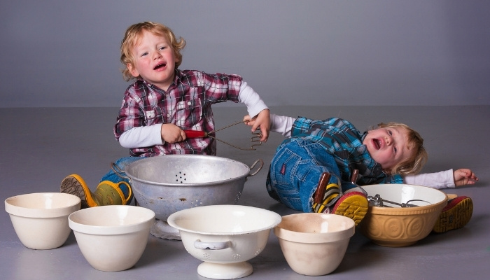 Toddler twin brothers arguing and crying over cooking utensils offered for playtime.