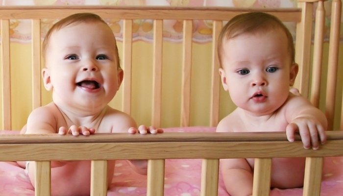 Cute twin babies on their tummies in their crib.
