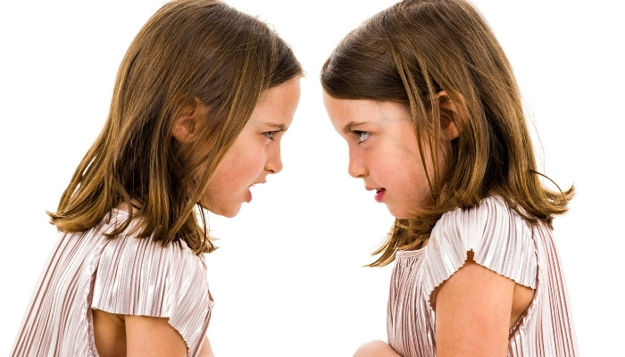 Identical twin sisters facing each other looking angry.