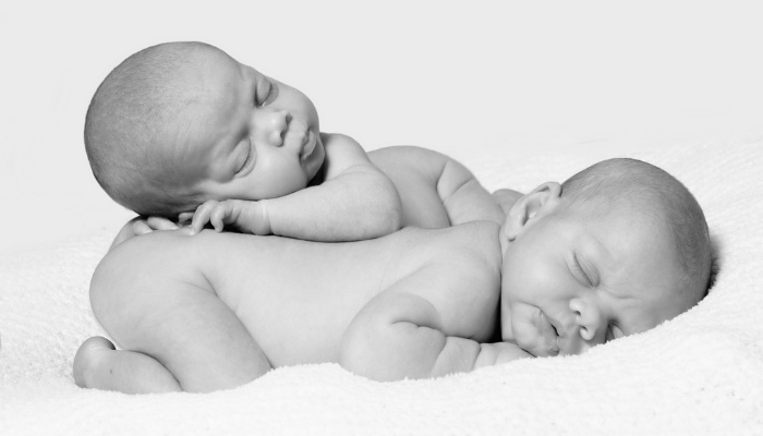 Naked twin babies sleeping with one on top of the other in black and white.