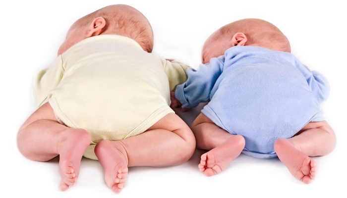 A set of newborn twins on their tummies with their bottoms facing the camera.