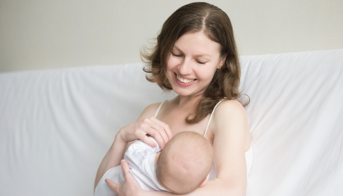 A young mother breastfeeding her baby against a white background.