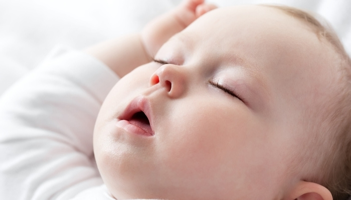 A baby sleeping peacefully with arms raised above his head.