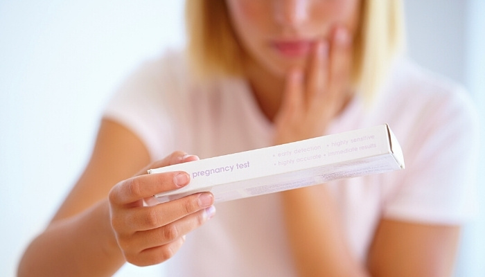 A woman looking confused and worried while reading the back of an unopened pregnancy test.