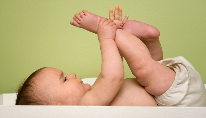 A cute baby lying on a changing table while wearing a cloth diaper and playing with his feet.