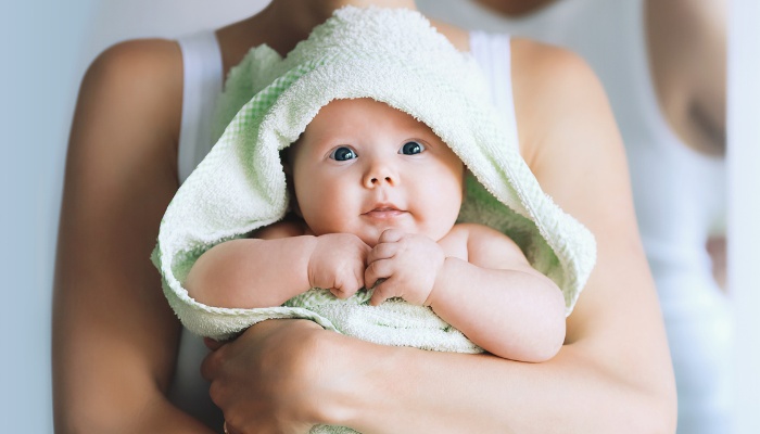 A baby wrapped in a bath towel being held in her mother's arms.
