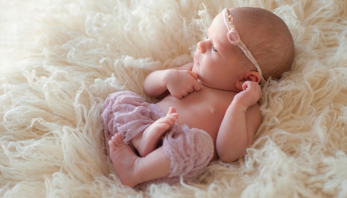 A shirtless newborn girl in pink pants lying on a furry white blanket.