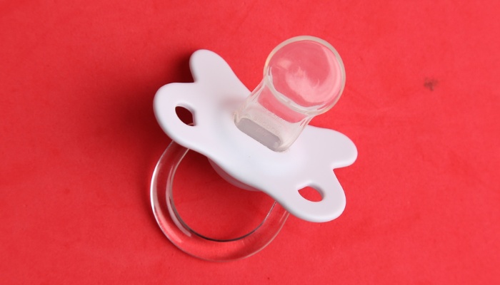 A baby pacifier against a red background.