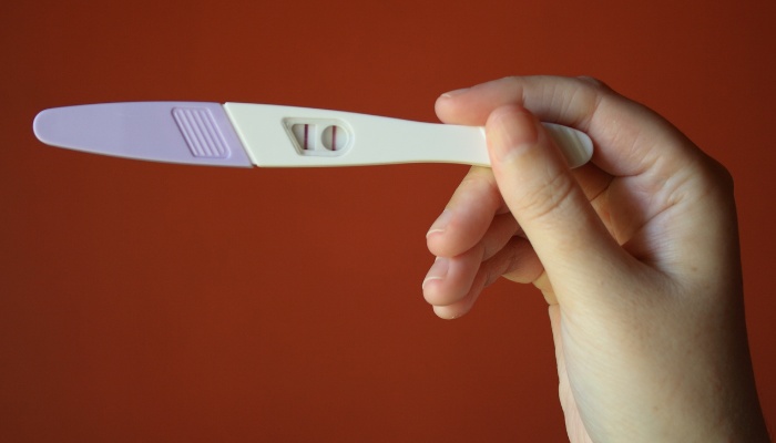 A woman's hand holding a pregnancy test against a brown background.