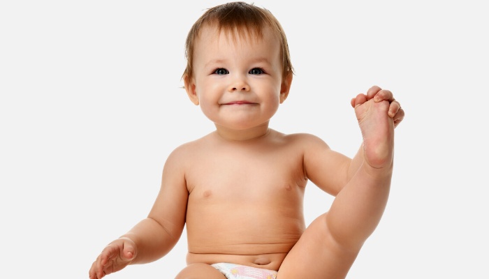 A cute toddler in a diaper holding up one of his legs.