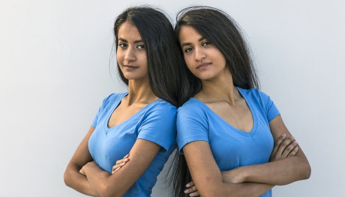 Adult twin sisters wearing matching blue shirts and standing back to back.