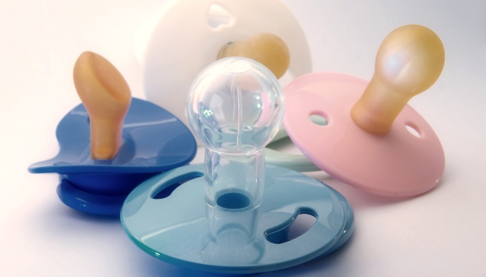 Four baby pacifiers of different types and colors on display.