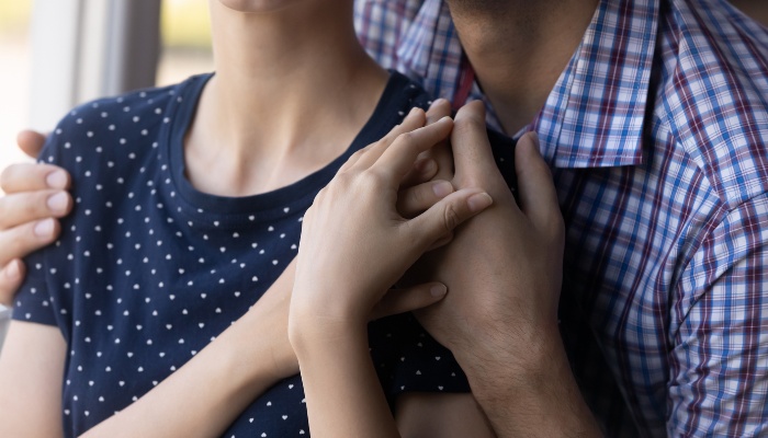 A husband stands behind his wife being supportive and offering comfort.