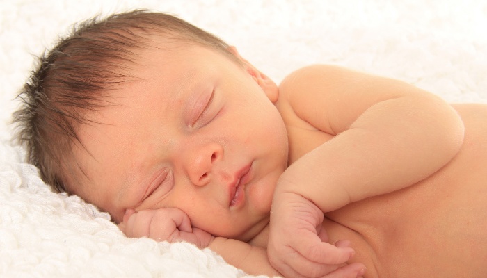 A newborn baby boy asleep on his side on a white blanket.