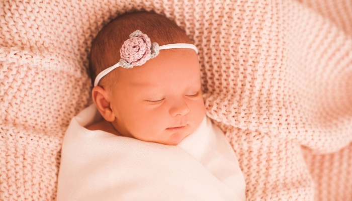 A cute baby girl in pink swaddled snugly and wearing a rose headband.