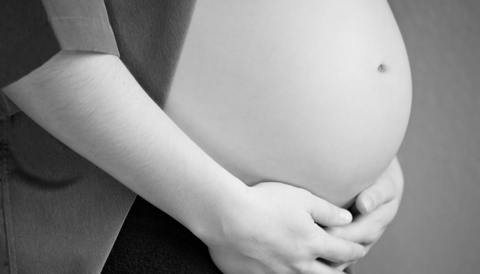 Black-and-white image of a woman linking her hands beneath her large pregnant belly.