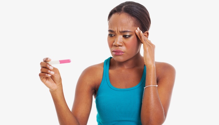 A woman in a blue tank top holding a pregnancy test and looking confused.