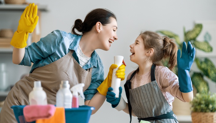 A lady and girl having fun and singing while cleaning the house.