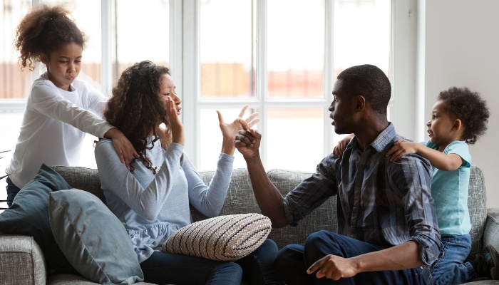 Two parents having an argument on the couch while their children try to intercede.