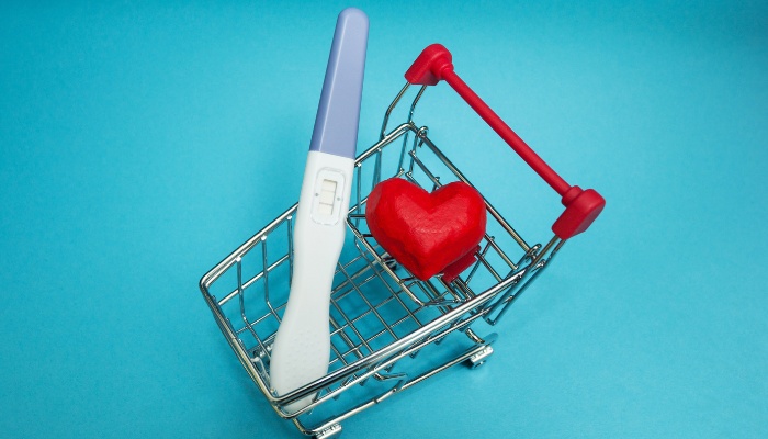 A pregnancy test and a red heart in a miniature shopping cart.