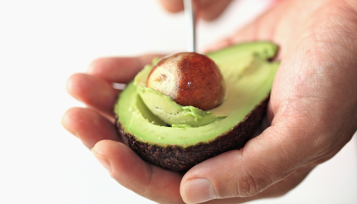 A man using a nut pick to remove the seed from an avocado.