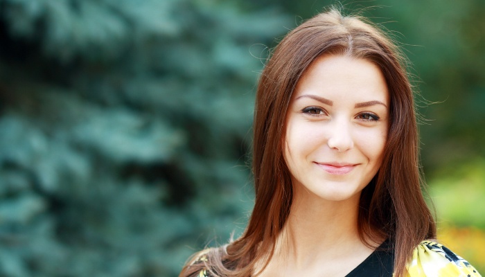 A woman standing outdoors with a cool, confident smile on her face.