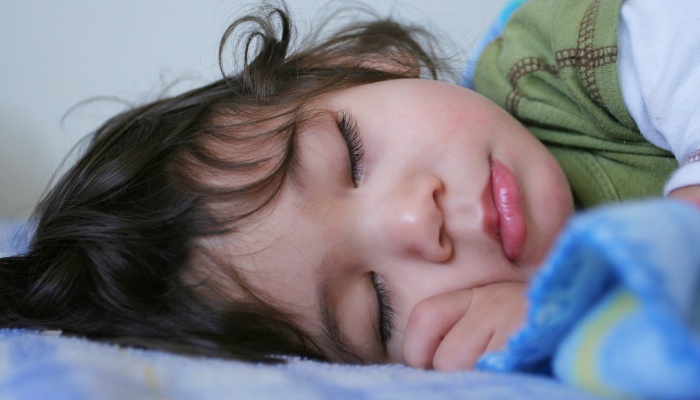 A toddler lies fast asleep under a blue blanket.