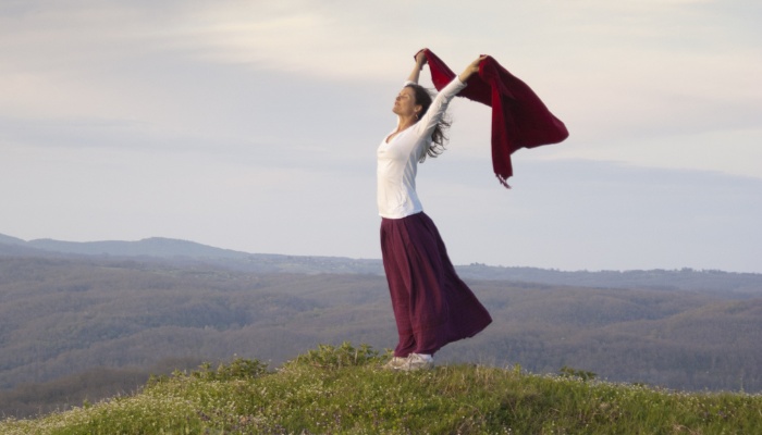 A woman standing on a mountaintop holding her sweater above her head to blow in the breeze.