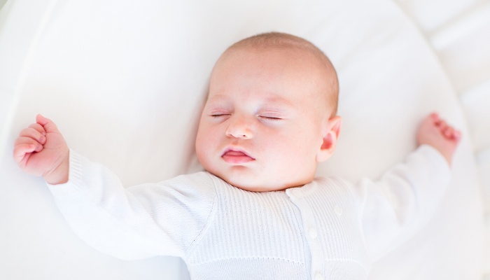 A baby is sound asleep in a white bassinet.