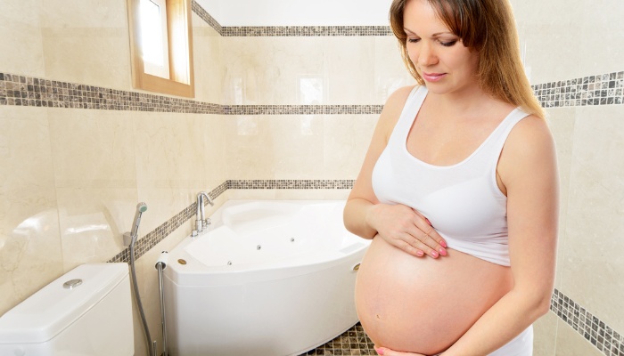 A pregnant woman standing in her bathroom looking thoughtful.