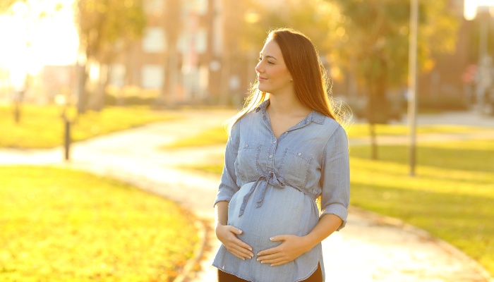 A happy pregnant woman walking along a path in a park at sunset.