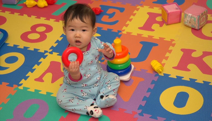 A young baby playing alone on an alphabet mat at a daycare.