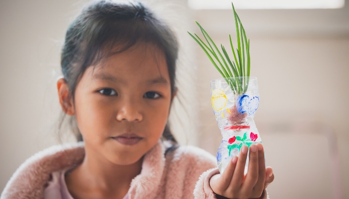 A young girl showing the bulb she is growing in a hand-painted plastic bottle.
