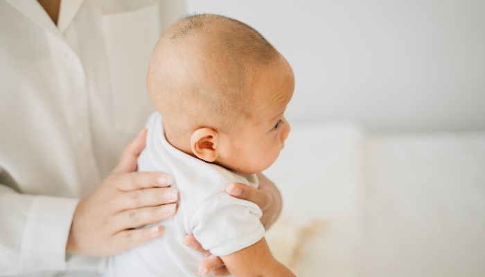 A newborn baby being burped while sitting up.