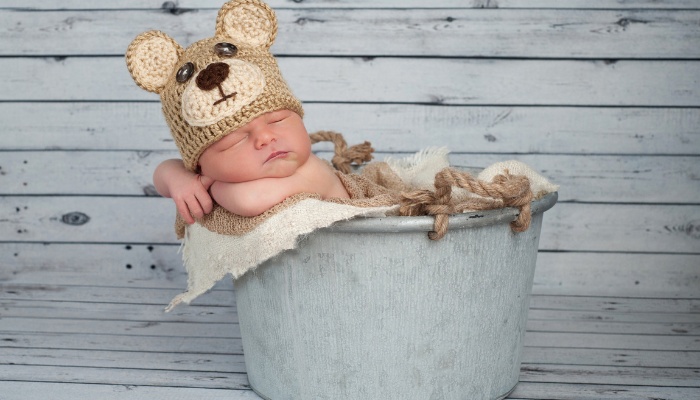 A newborn posed in a metal tub and cute hat for a photo shoot.