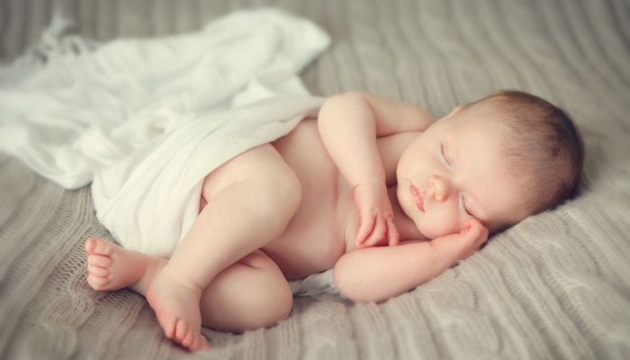 A newborn posed on a bed with a white blanket.
