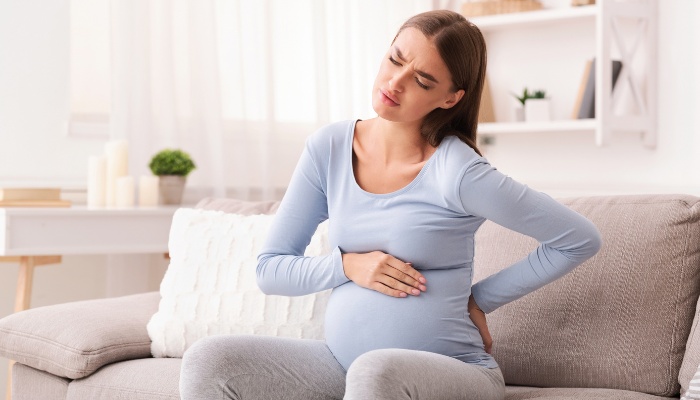 A pregnant lady sitting on a couch rubbing her sore back.