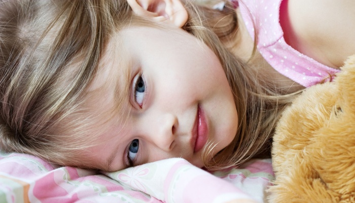 A cute little girl lying on her side in bed with a teddy bear.