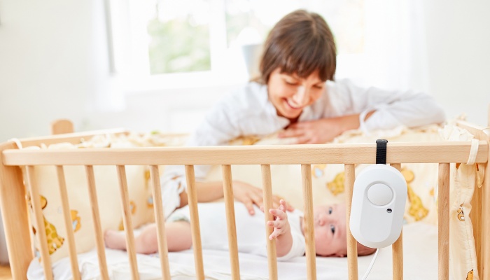 A baby monitor hanging on a baby crib while mother puts baby to bed.