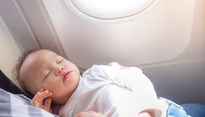 A baby sleeping peacefully in mother's arms on an airplane.